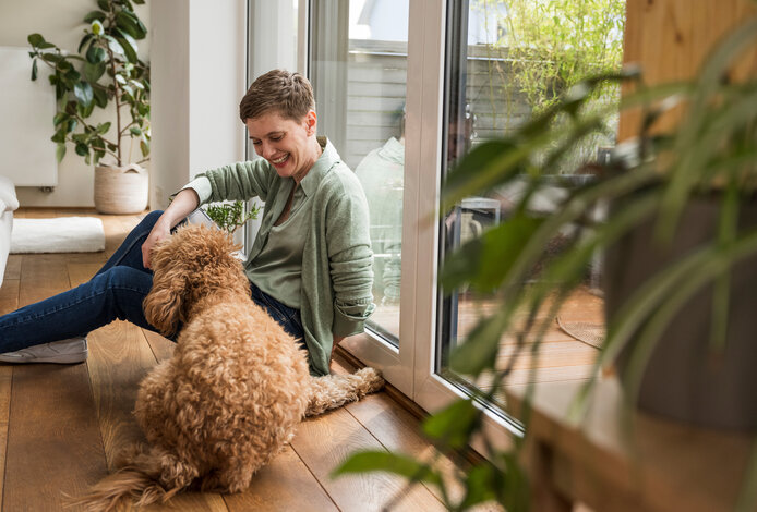 Eine lächelnde Frau mit ihrem Hund in einem gemütlich beheizten Wohnraum – Symbolbild für die Effizienz und Behaglichkeit durch schwefelarmes Heizöl