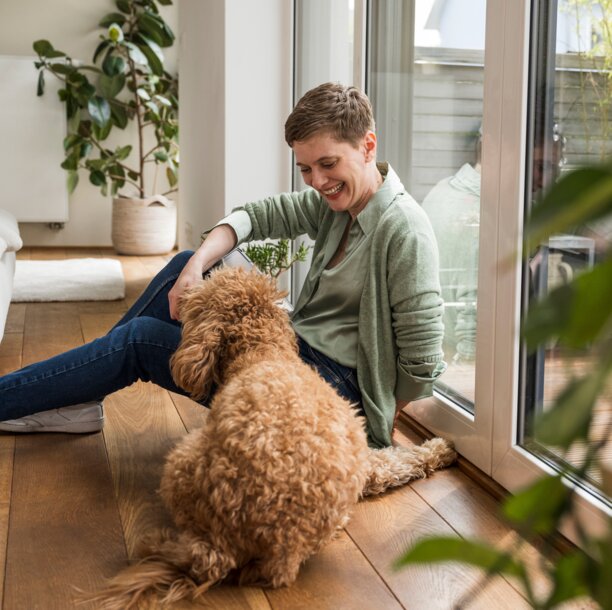 Eine lächelnde Frau mit ihrem Hund in einem gemütlich beheizten Wohnraum – Symbolbild für die Effizienz und Behaglichkeit durch schwefelarmes Heizöl