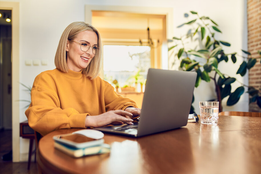 Lächelnde Frau arbeitet zu Hause am Laptop – Beispielrechnung für Kosten und Förderungen der Heizungsmodernisierung 2026