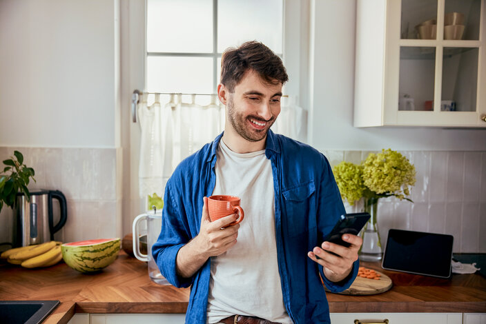 Mann in der Küche prüft Preise auf dem Smartphone – Informationen zu Risiken und Preisschwankungen beim dynamischen Stromtarif