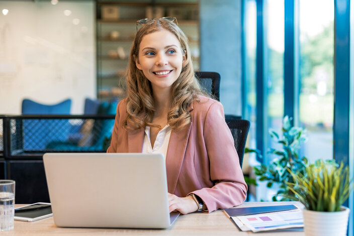 Eine lächelnde Geschäftsfrau arbeitet am Laptop in einem modernen Büro – Informationen zur schrittweisen Pflicht für elektronische Rechnungen im B2B-Bereich ab 2025