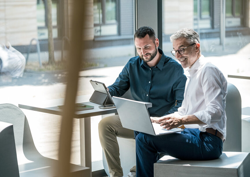 Zwei Männer besprechen entspannt Daten an einem Laptop – Kostenlose Energieberatung durch MONTANA zur Senkung von Heizkosten