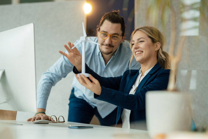 Zwei Geschäftspartner betrachten lächelnd ein Modell eines Windrads – Jetzt individuellen Strompreis im MONTANA Gewerbestrom-Tarifrechner berechnen