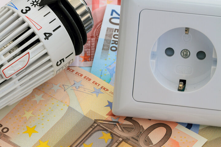 Symbolbild für die Grundversorgung bei Strom und Gas: Steckdose, Heizungsthermostat und Euro-Scheine