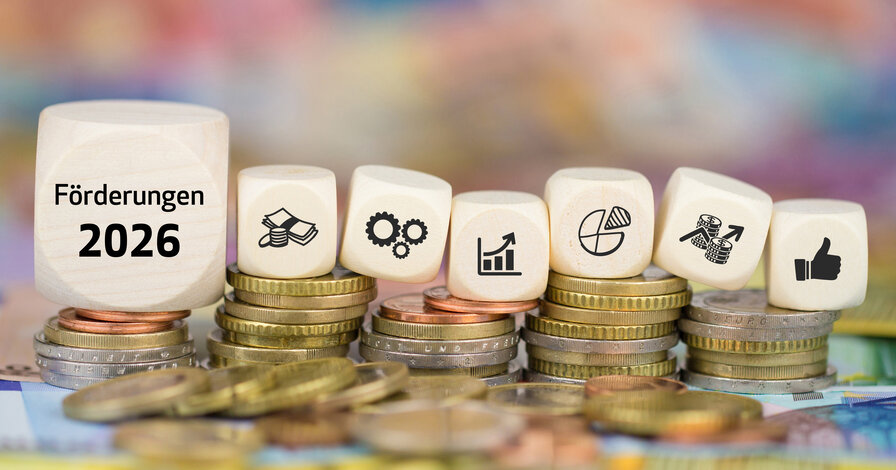 Weiße Würfel mit der Aufschrift 'Förderungen 2026' und Finanz-Icons auf gestapelten Euro-Münzen – Ratgeber zu staatlichen Zuschüssen für klimafreundliche Heizungen