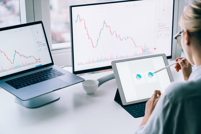Person analysiert Kursentwicklungen und Diagramme an mehreren Bildschirmen – Ratgeber zu wirtschaftlicher Energieversorgung und flexiblen Tarifen