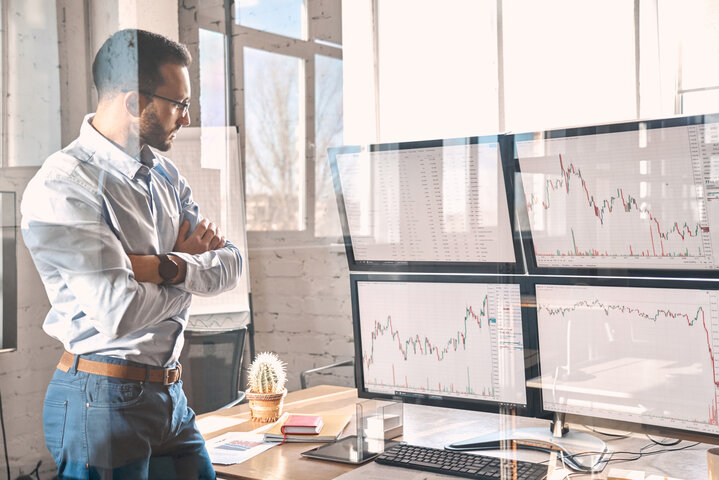 Ein nachdenklicher Mann betrachtet Kursentwicklungen an mehreren Monitoren – Ratgeber zu Fixpreisen und der Energiebeschaffung für Immobilien