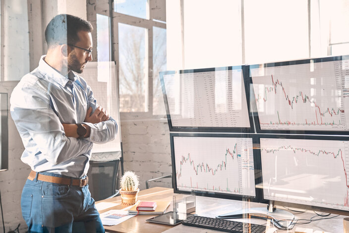 Ein nachdenklicher Mann betrachtet Kursentwicklungen an mehreren Monitoren – Ratgeber zu Fixpreisen und der Energiebeschaffung für Immobilien