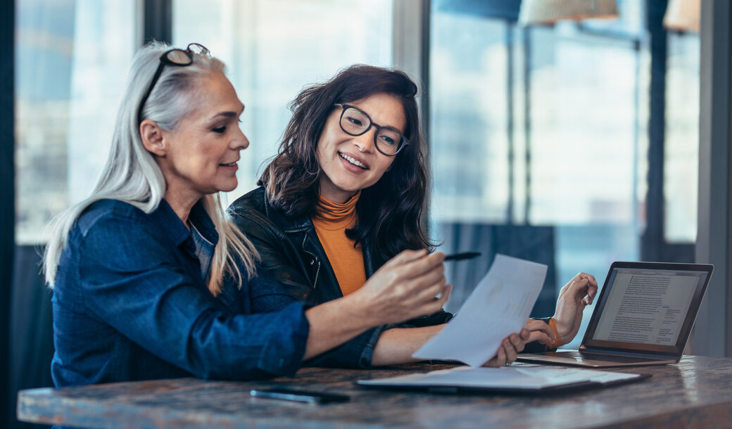 Zwei Frauen besprechen gemeinsam ein Dokument an einem Tisch mit Laptop – Anmeldung zum kostenlosen MONTANA Energiebrief für aktuelle Preisentwicklungen am Energiemarkt
