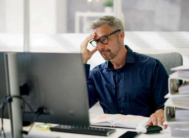 Ein gestresster Mitarbeiter sitzt vor dem Computerbildschirm im Büro – Lösungen gegen den Fachkräftemangel in Hausverwaltungen