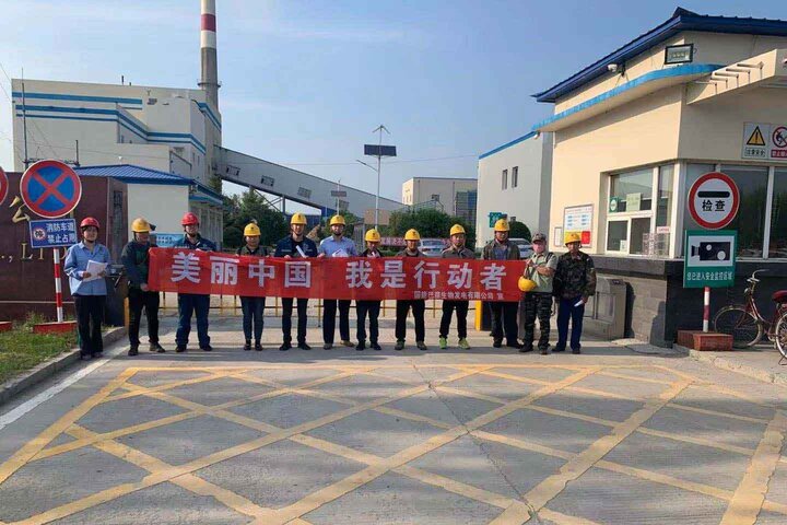 Eine Gruppe von Arbeitern mit Schutzhelmen hält ein Banner vor einem Biomassekraftwerk in China – MONTANA Klimaschutzprojekt 2026