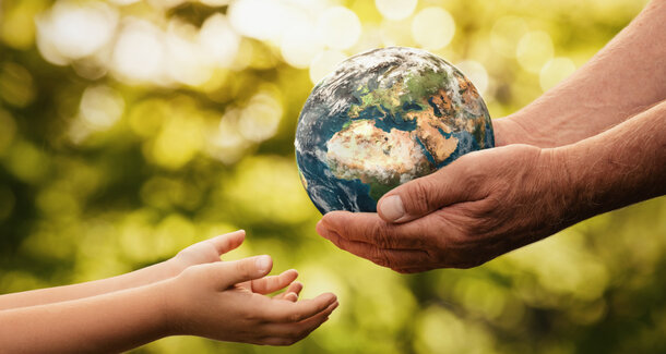 Erwachsene Hände übergeben eine Weltkugel an Kinderhände in der Natur – Stromspartipps für mehr Klimaschutz und einen geringeren Energieverbrauch