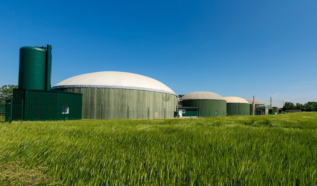 Moderne Biogasanlage mit grünen Behältern an einem Getreidefeld – Erdgas mit Biogas-Anteil von MONTANA