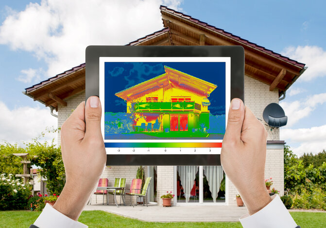 Hände halten ein Tablet mit einer Wärmebildaufnahme eines Hauses – Service zur Erstellung des Energieverbrauchsausweises