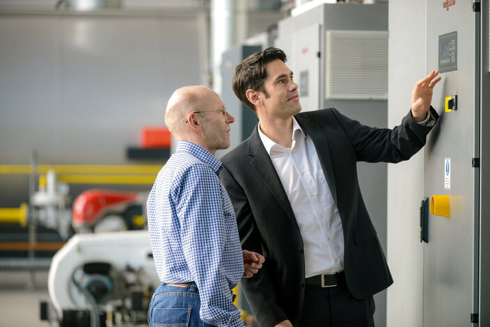 Experte und Kunde überprüfen die Steuerung einer großen Heizungsanlage – Infos zu Wartungsvertrag und 24-Stunden-Notdienst