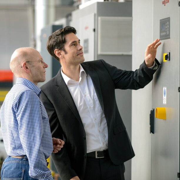 Experte und Kunde überprüfen die Steuerung einer großen Heizungsanlage – Infos zu Wartungsvertrag und 24-Stunden-Notdienst