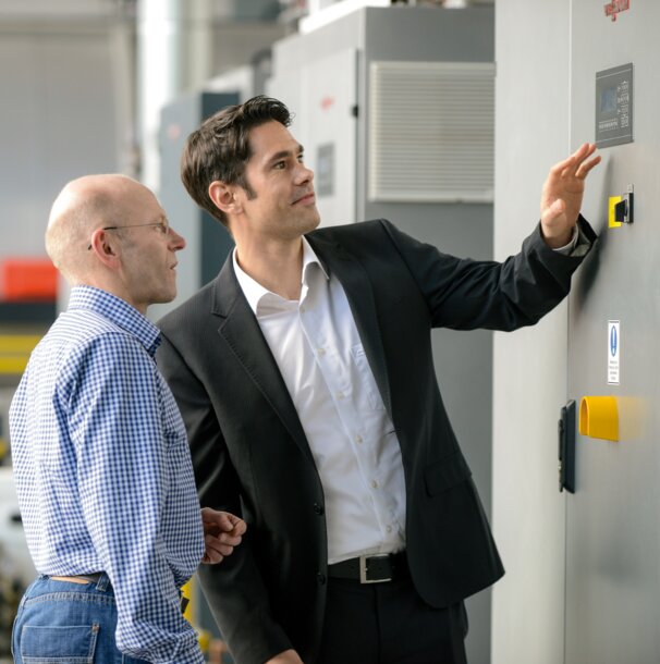 Experte und Kunde überprüfen die Steuerung einer großen Heizungsanlage – Infos zu Wartungsvertrag und 24-Stunden-Notdienst