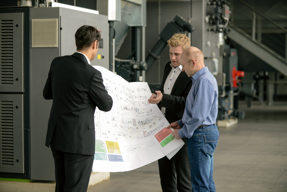 Drei Experten besprechen Baupläne in einer Industrieanlage – Beratung und Planung für Heiz- und Klimasysteme in Gewerbeimmobilien