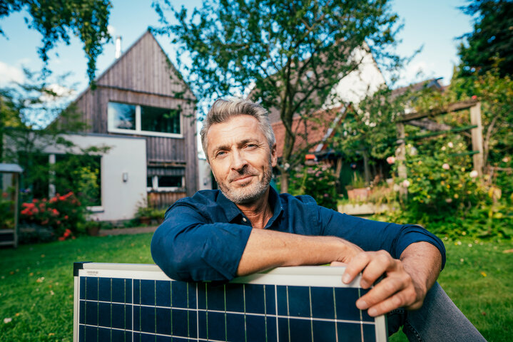 Ein zufriedener Hausbesitzer lehnt in seinem Garten an einem Solarmodul – Ratgeber zur Kombination von Wärmepumpe und Photovoltaik