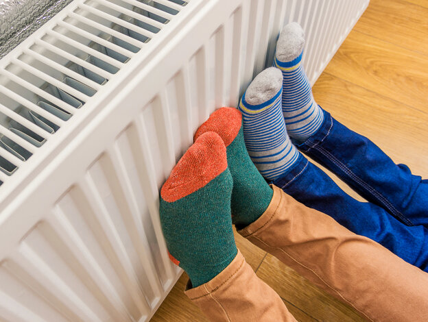 Zwei Paar Füße in dicken Socken wärmen sich an einem Heizkörper – Hilfreiche Energiespartipps, um Heizöl und Heizkosten zu sparen