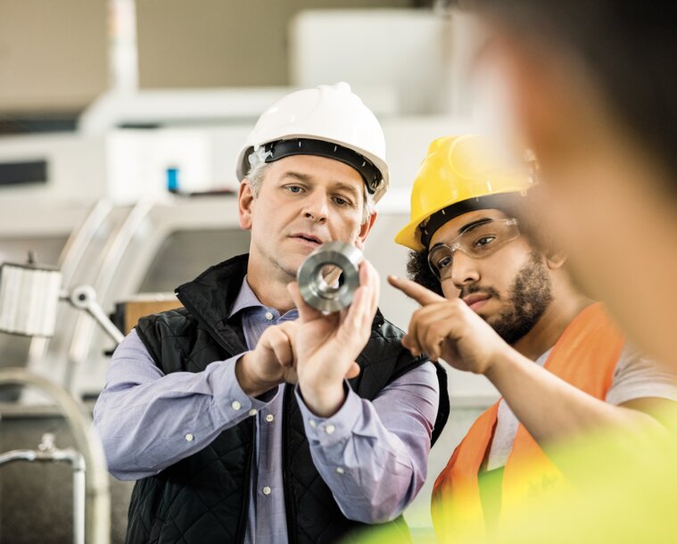 Zwei Fachkräfte mit Schutzhelmen begutachten gemeinsam ein metallisches Bauteil – Überblick der Vorteile wie persönliche Beratung und maßgeschneiderte Schmierstoff-Lösungen