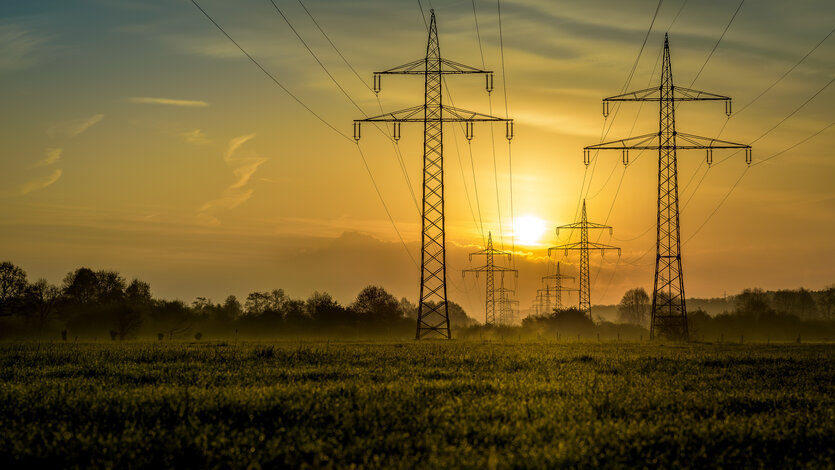 Hochspannungsmasten und Stromleitungen bei Sonnenuntergang – MONTANA Gewerbestromtarife für Unternehmen und Selbstständige