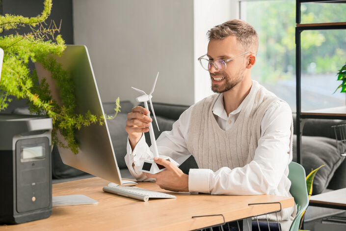 Mann am Schreibtisch hält ein kleines Windrad – Ökostrom Standard aus 100 % erneuerbaren Energien