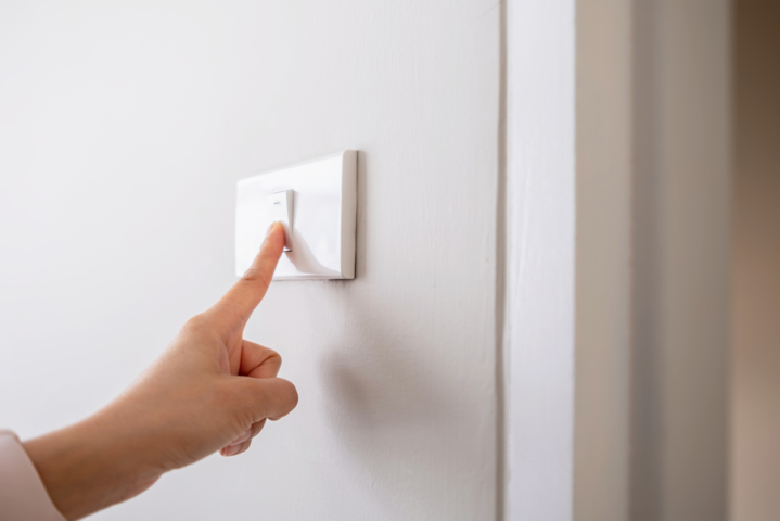 Hand schaltet das Licht am Lichtschalter an einer weißen Wand aus, um Strom zu sparen.