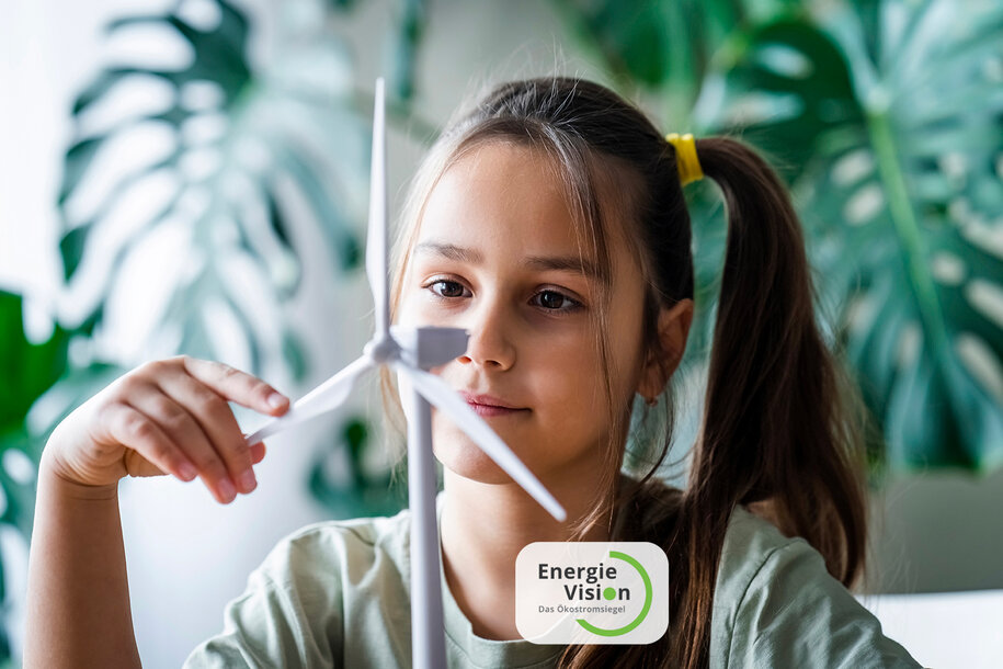Mädchen betrachtet interessiert ein Modell-Windrad; EnergieVision - das Ökostromsiegel im Vordergrund