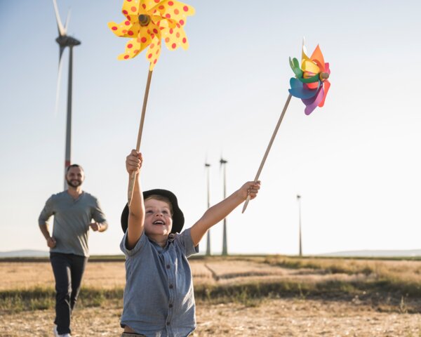 Kind spielt mit bunten Windrädern auf einem Feld, im Hintergrund Windkraftanlagen