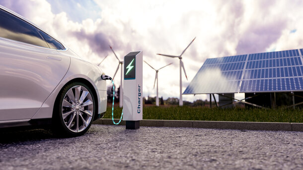 Ein weißes Elektroauto lädt an einer Ladesäule vor Solarpanels und Windkraftanlagen – Häufige Fragen zum Verkauf der THG-Quote und der THG-Prämie