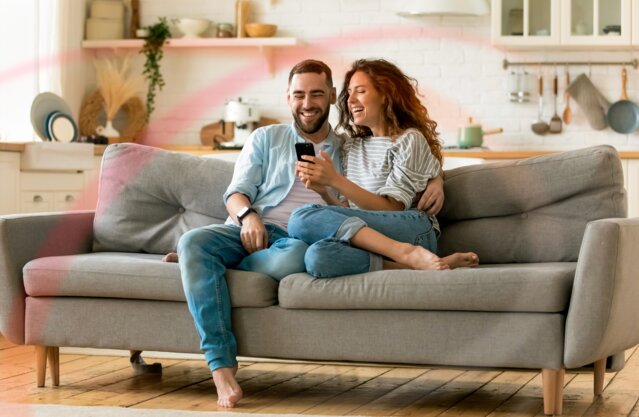 Lachendes Paar auf dem Sofa schaut auf ein Smartphone – attraktive MONTANA Stromtarife
