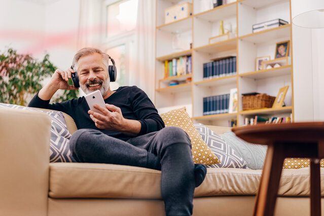 Ein entspannter Mann nutzt sein Smartphone mit Kopfhörern auf dem Sofa – Mit wenigen Klicks zum optimalen Stromtarif im MONTANA Tarifrechner