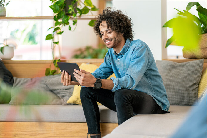 Ein lächelnder junger Mann nutzt ein Tablet in einer grünen, hellen Umgebung – MONTANA Erdgastarife mit Biogas-Anteil für nachhaltiges Heizen