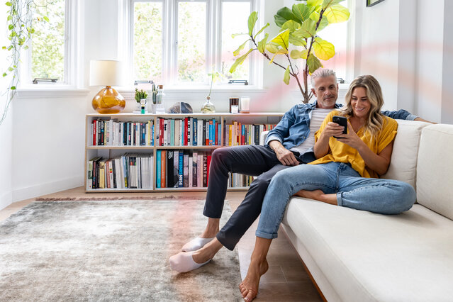 Paar im hellen Wohnzimmer wählt Gastarif auf dem Smartphone – Anmeldung für Neukunden bei Neueinzug