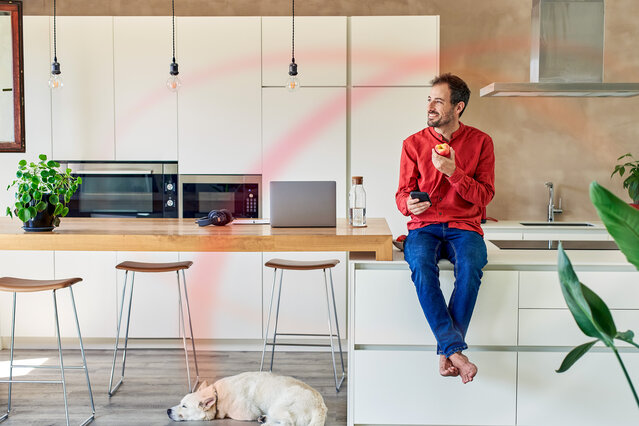 Mann mit Apfel in der Küche schaut auf ein Smartphone – Tarifrechner für den optimalen Erdgastarif starten