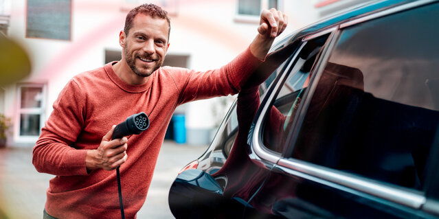 Lächelnder Mann mit Ladekabel am Elektroauto – E-Mobility Lösungen und Ladestrom von MONTANA