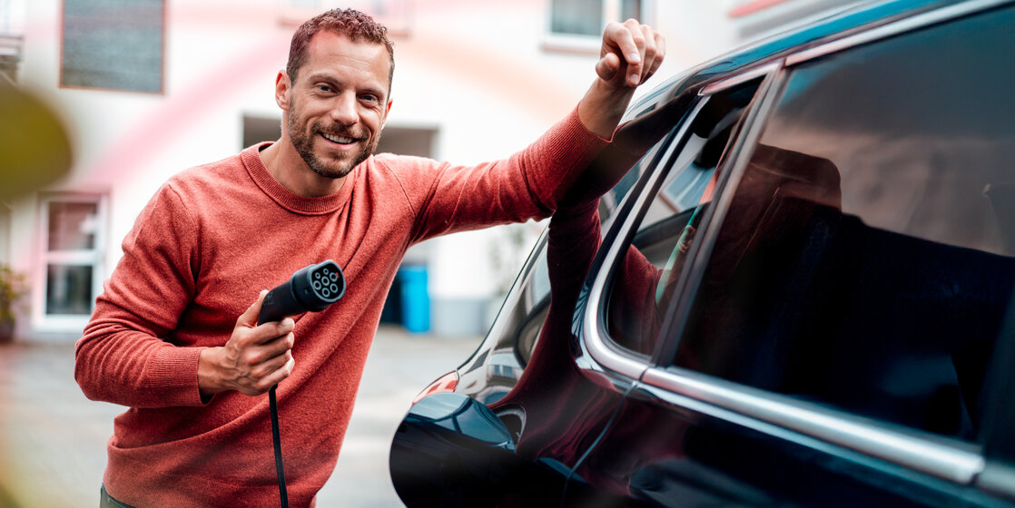 Lächelnder Mann mit Ladekabel am Elektroauto – E-Mobility Lösungen und Ladestrom von MONTANA