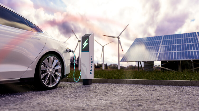 Ein weißes Elektroauto lädt an einer Ladesäule vor Solarpanels und Windkraftanlagen – Häufige Fragen zum Verkauf der THG-Quote und der THG-Prämie