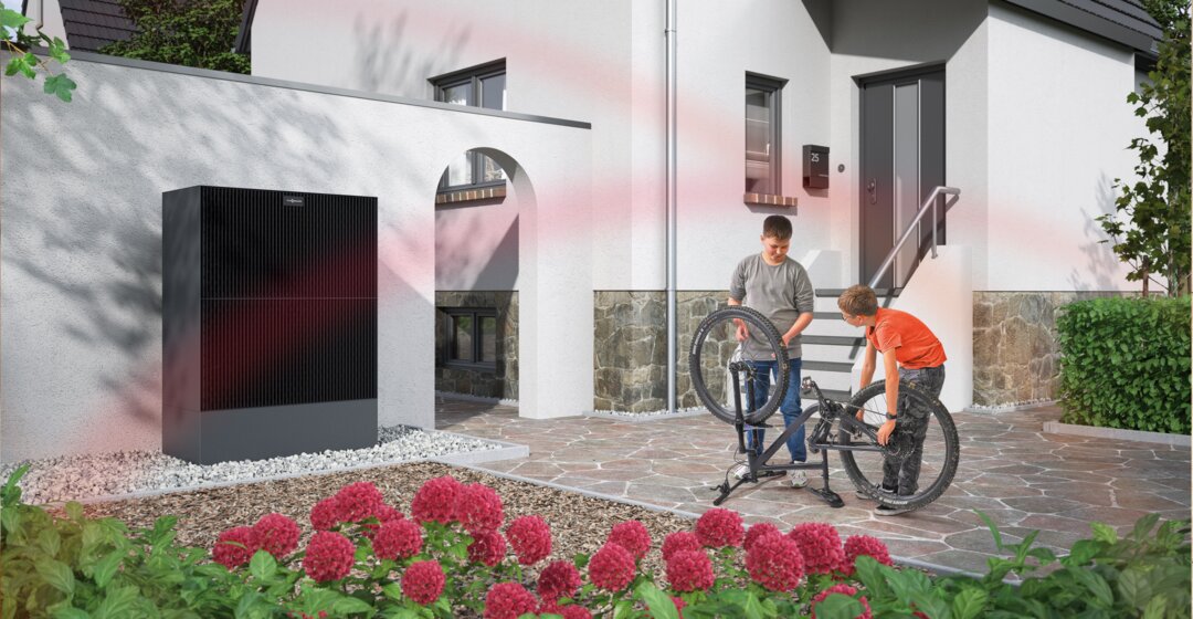 Eine moderne Wärmepumpe an der Außenwand eines Wohnhauses, im Hintergrund reparieren zwei Kinder ein Fahrrad – MONTANA Wärmepumpen-Lösungen für Bestandsgebäude