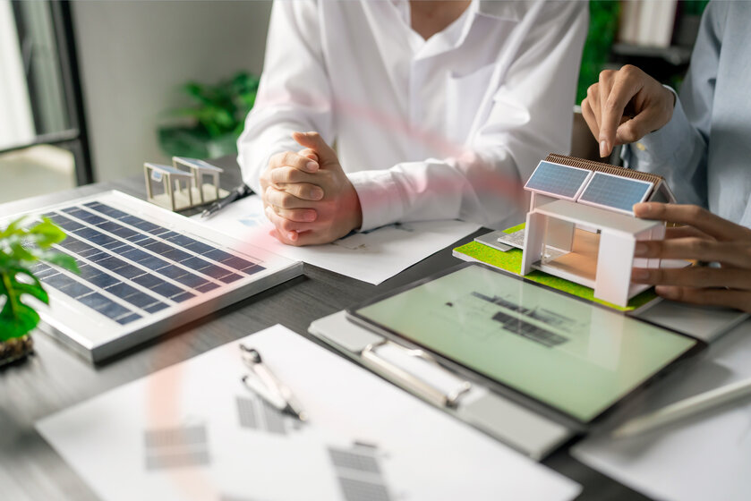 Beratung am Schreibtisch mit kleinen Hausmodellen mit Solardach – Planung und Berechnung der Wirtschaftlichkeit einer PV-Anlage mit Stromspeicher