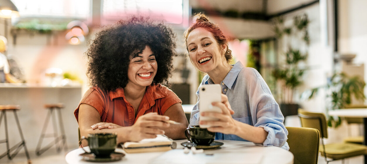 Zwei Freundinnen lachen gemeinsam über ein Smartphone – MONTANA Kunden werben Kunden Empfehlungsprogramm für Ökostrom und Erdgas