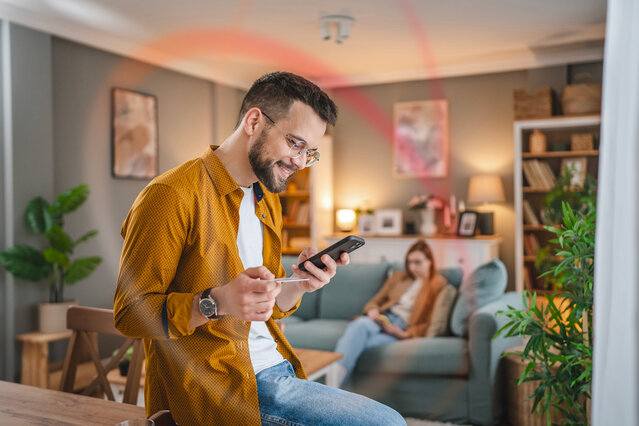 Mann im Wohnzimmer gibt Daten in sein Smartphone ein – Online-Stromanmeldung für Neukunden