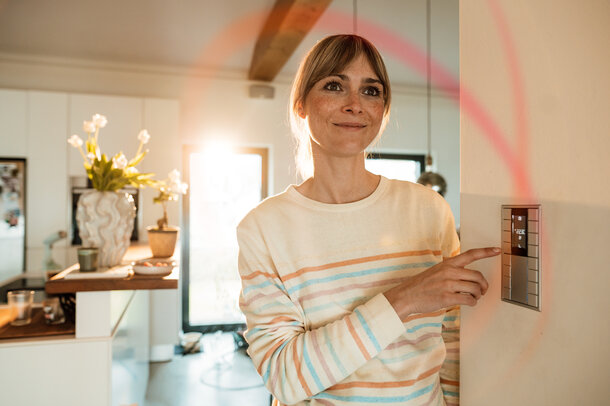 Eine Frau blickt im gemütlich beleuchteten Wohnzimmer auf ein Elektrogerät – Tarifrechner für den dynamischen Stromtarif MONTANA ÖkoStrom Plus