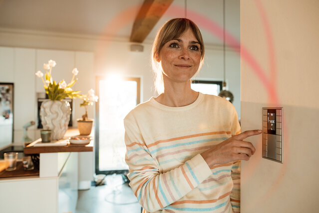 Eine Frau blickt im gemütlich beleuchteten Wohnzimmer auf ein Elektrogerät – Tarifrechner für den dynamischen Stromtarif MONTANA ÖkoStrom Plus