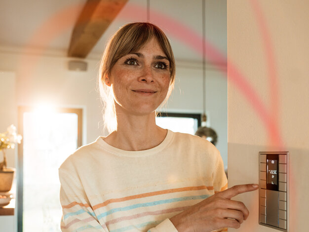 Eine Frau blickt im gemütlich beleuchteten Wohnzimmer auf ein Elektrogerät – Tarifrechner für den dynamischen Stromtarif MONTANA ÖkoStrom Plus