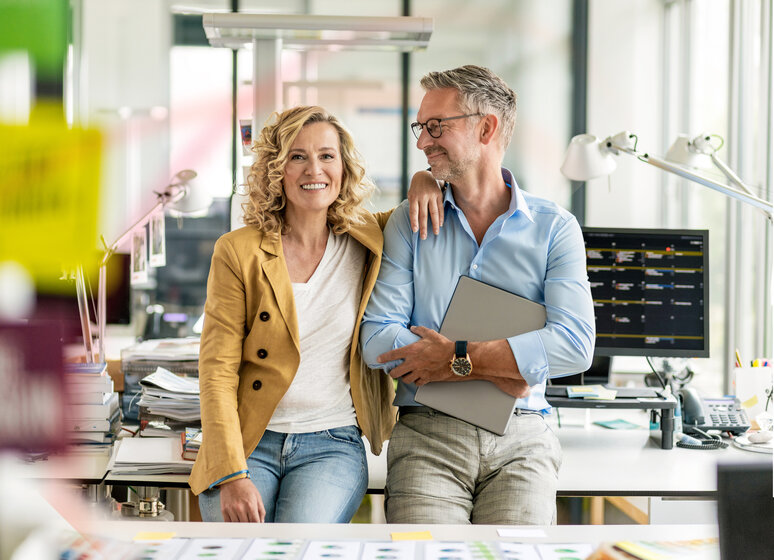 Zwei Geschäftspartner lächeln sich in einer modernen Büroumgebung an – Zuverlässige Energieversorgung mit Strom und Gas für Gewerbekunden von MONTANA