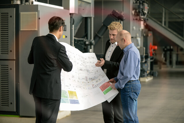 Drei Experten besprechen Baupläne in einer Industrieanlage – Beratung und Planung für Heiz- und Klimasysteme in Gewerbeimmobilien