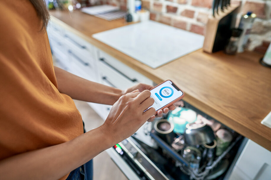 Person prüft Strompreis-App vor der offenen Spülmaschine – intelligente Gerätenutzung mit dem dynamischen Stromtarif