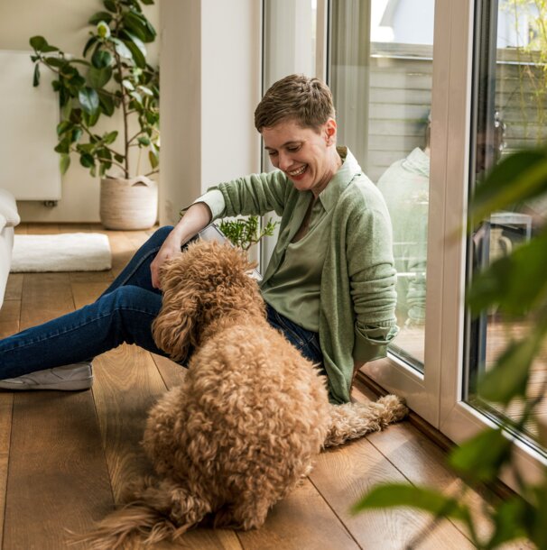 Entspannte Frau genießt mit ihrem Hund die Wärme im gemütlichen Zuhause – Strom für Wärmepumpen